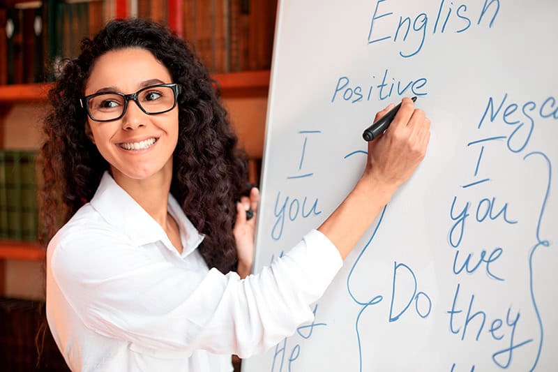 Fotografía de una instructora escribiendo una lección de inglés en pizarrón, relacionada con cursos intensivos para adultos.