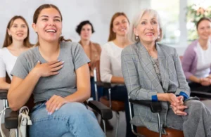 Mujer joven riendo en una clase de ingles junto a compañeras adultas mayores sentadas en sillas.