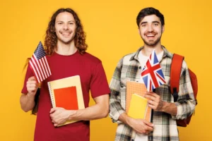 Dos estudiantes universitarios sonrientes sostienen banderas de EE. UU. y Reino Unido sobre fondo amarillo brillante.