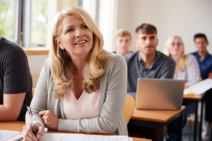 Mujer rubia adulta tomando notas en una clase de inglés con otros estudiantes de fondo