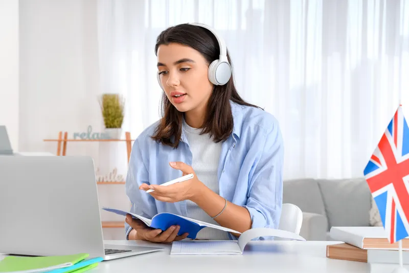 Estudiante con audífonos frente a laptop tomando notas durante clase de inglés online.